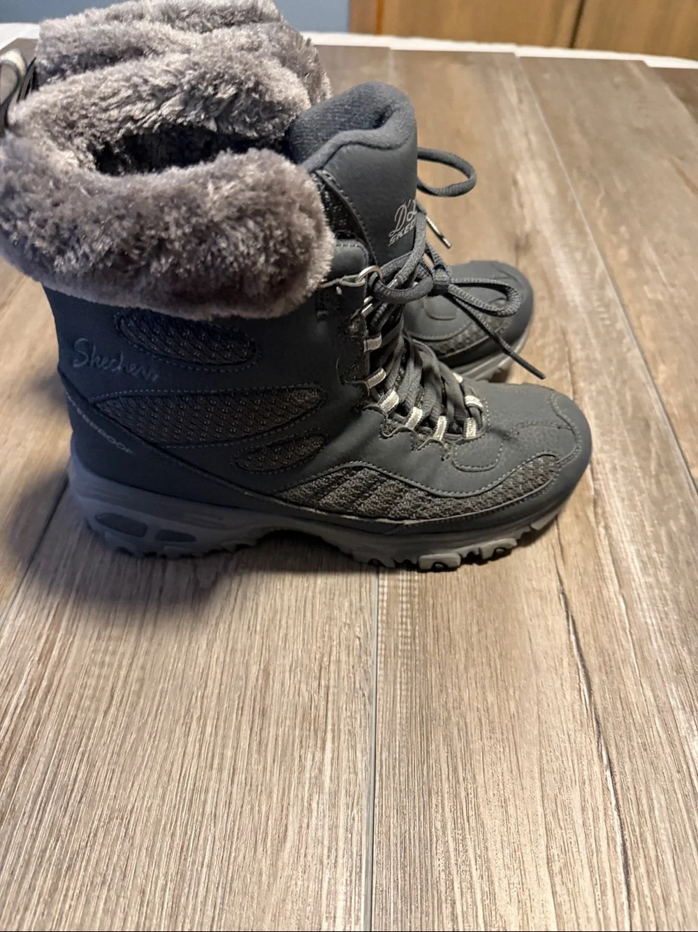 Skechers D'Lites Bomb Cyclone winter boots in a charcoal color, featuring a faux